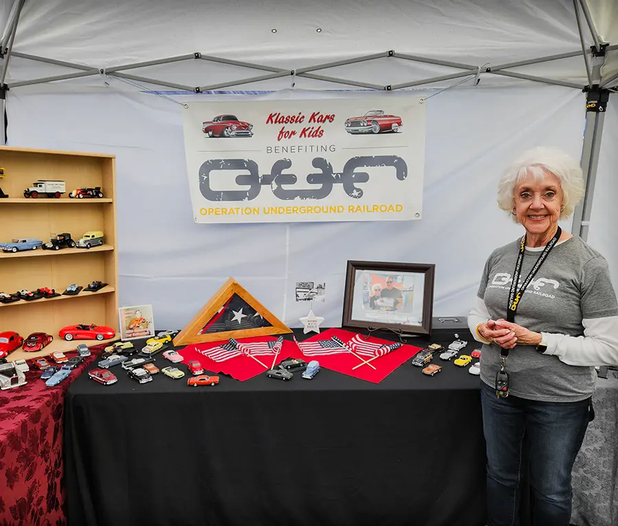 A woman stands infront of a table with collectible toy cars to raise funds for OUR Rescue