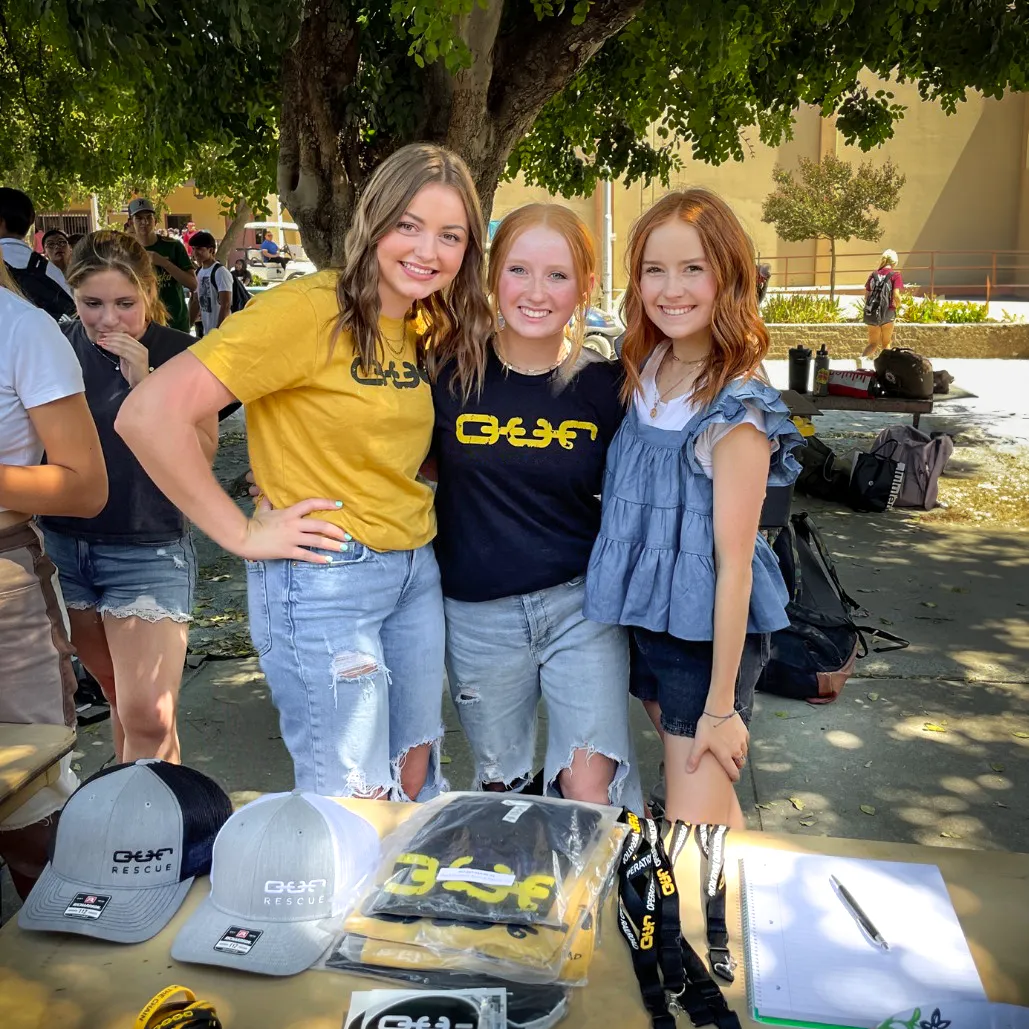 3 girls pose behind a table of OUR Rescue info at a highschool