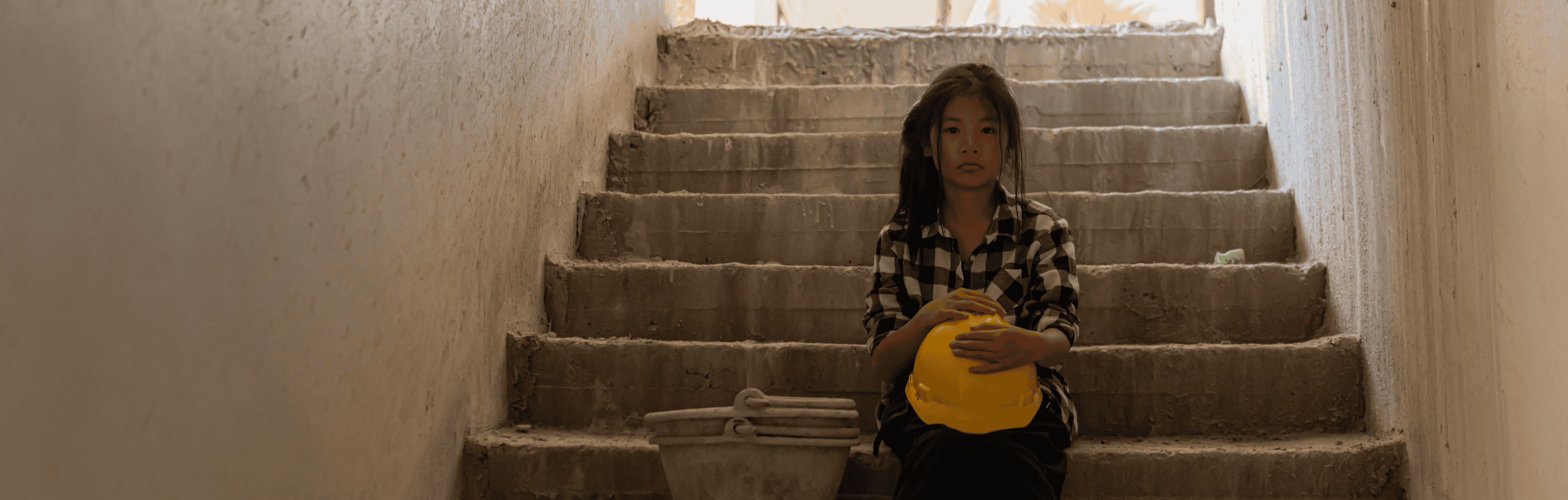 A girl sits on steps holding a construction hat