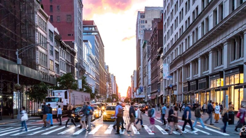 very busy city street filled with people walking across the sreet.