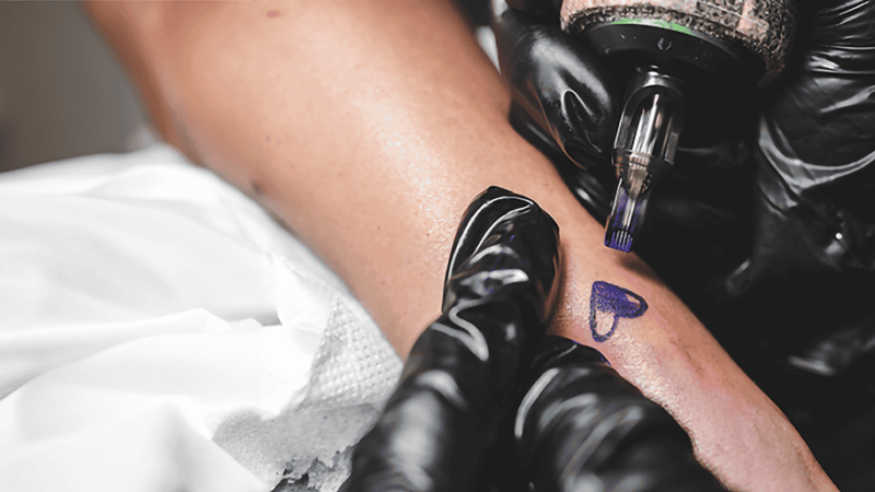 A woman's arm is being tattooed with a heart