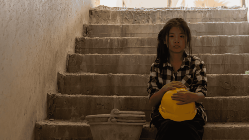 A girl sits on steps holding a construction hat
